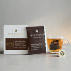 Ember Roast Black Tea sachets box and sealed sachet wrapper beside a glass cup of freshly brewed tea