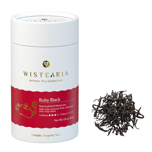 Wistearia Ruby Black Tea loose leaf tube beside a pile of long twisted whole leaves
