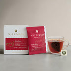 Ruby Black Tea sachets box and sealed sachet wrapper beside a glass cup of freshly brewed tea